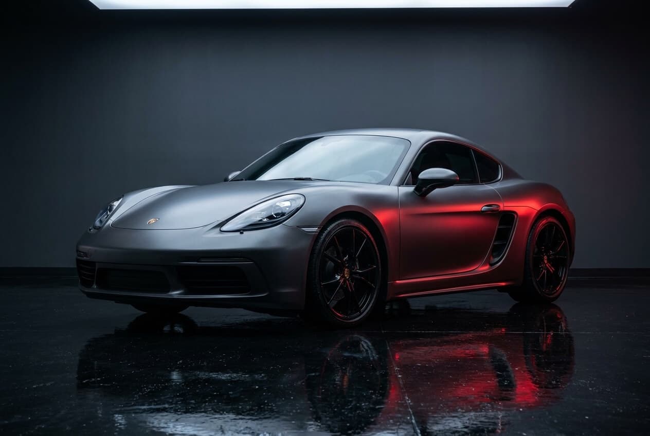 Photoreal render of a Porsche 718 Cayman in a satin gray-to-charcoal color-shift wrap.
